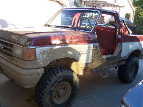 1991 Ford Bronco - Mud-splattered 1991 Ford Bronco with its doors removed sits in a driveway.