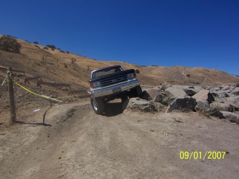 1991 Ford Bronco - A 1991 Ford F-Series truck navigates a rocky, off-road course under a clear blue sky.