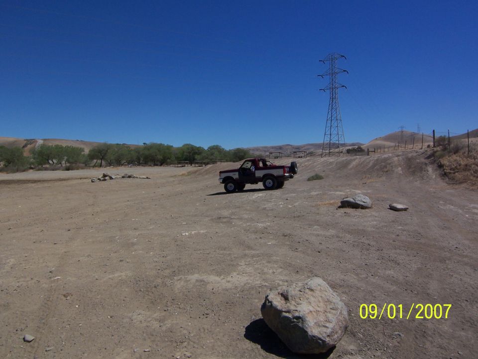 Red and white Ford Bronco parked on a dirt hill with a power tower in the background