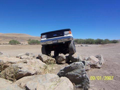 1991 Ford Bronco - A white 1991 Ford Bronco navigates a rocky obstacle course under a clear blue sky.