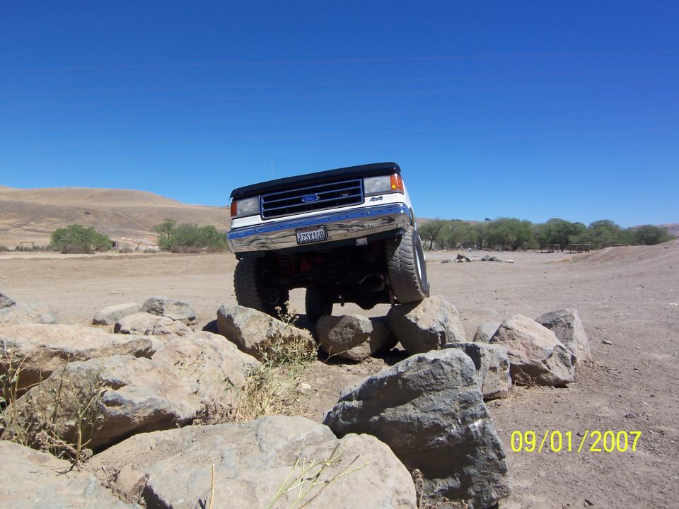 White 1991 Ford Bronco climbing over rocks on a dirt trail