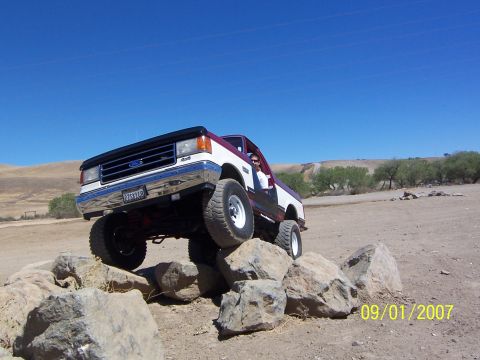1991 Ford Bronco - Ford F-Series truck navigating a rocky obstacle course on a sunny day.