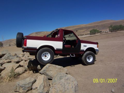 1991 Ford Bronco - A two-tone Ford Bronco is shown off-road with its doors removed.