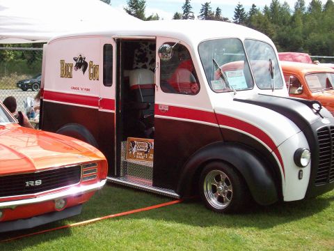 1997 Ford Mustang - A classic delivery truck with a unique paint scheme is parked on grass next to a muscle car.
