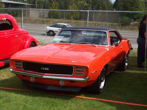 1997 Ford Mustang - A classic orange 1969 Chevrolet Camaro RS is displayed on a grassy field next to another vintage car.