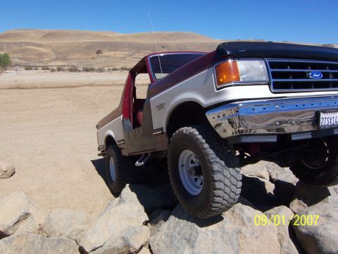 1991 Ford Bronco - This two-tone Ford Bronco is navigating a rocky trail under a clear blue sky.