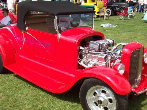 1997 Ford Mustang - A bright red convertible hot rod with a black soft top and a polished V8 engine is displayed on a grassy field.