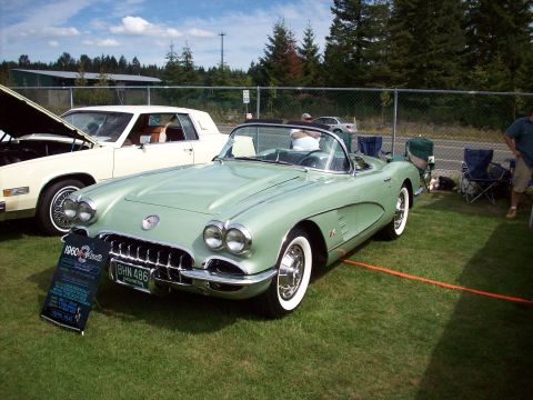 1997 Ford Mustang - A light green 1960 Chevrolet Corvette is displayed at an outdoor event, with a white coupe parked behind it.
