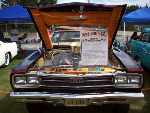 1997 Ford Mustang - A 1969 Plymouth GTX is displayed with its hood open, revealing the engine and a detailed information sign.