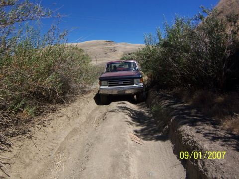 1991 Ford Bronco - Ford F-Series truck navigates a challenging dirt track under a clear blue sky.