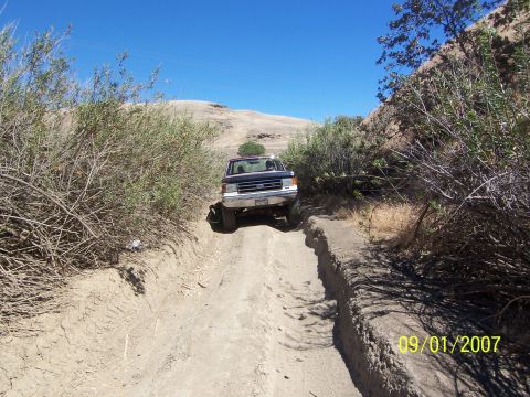 1991 Ford Bronco - A Ford F-Series truck navigates a rutted dirt track under a clear blue sky.