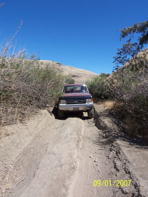 1991 Ford Bronco - A maroon Ford F-Series truck navigates a dirt path on a sunny day.