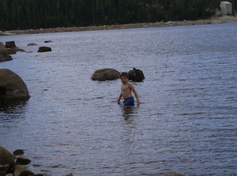 1986 Ford Bronco - A young boy stands in the water near rocks and tree stumps at a lake.