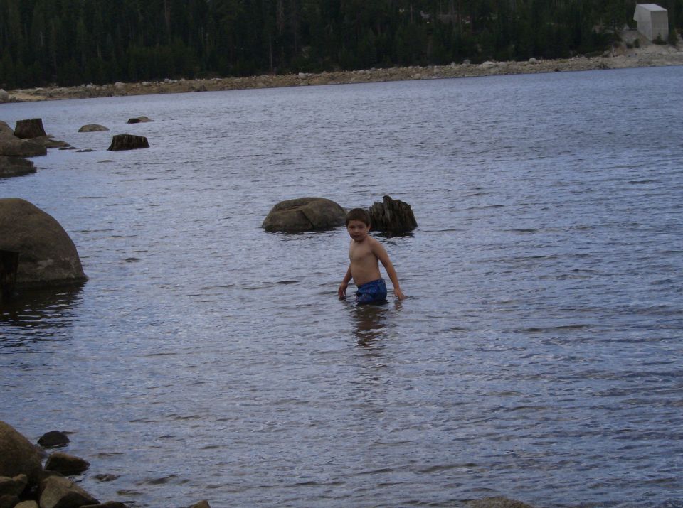 Child wading in a lake with trees and rocks in the background