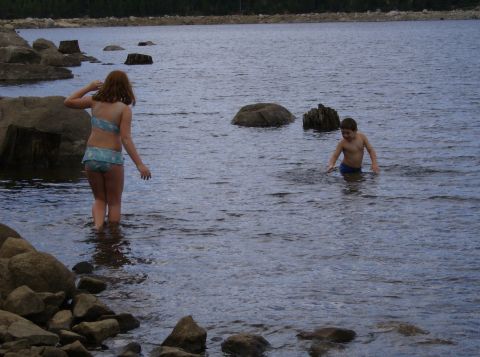1986 Ford Bronco - Two children enjoy a day at the lake, standing in the shallow water near the rocky shore.
