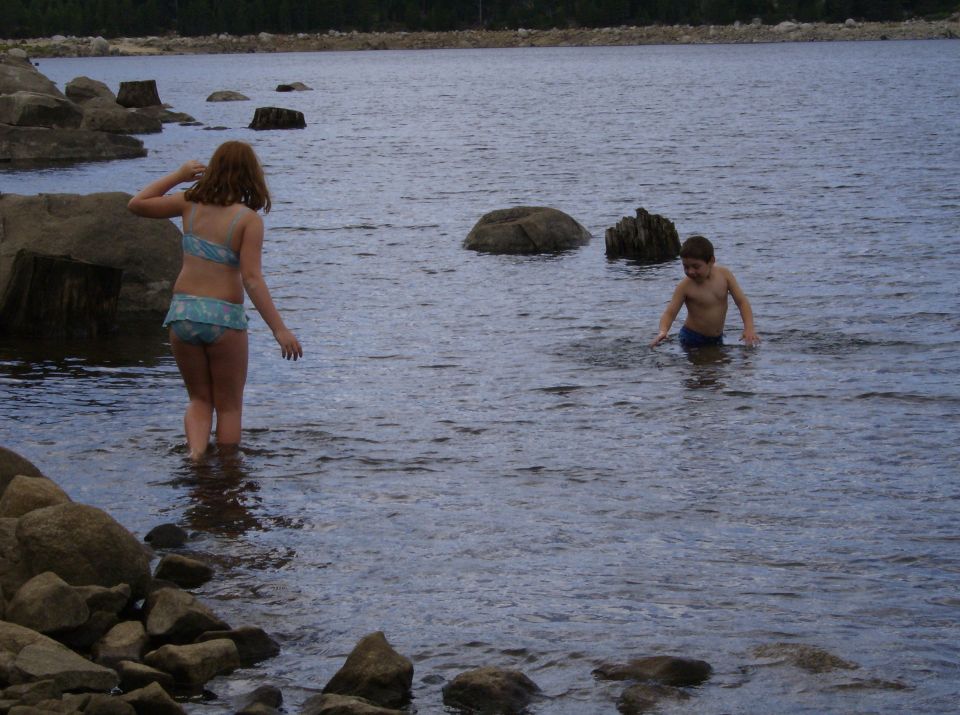 Kids wading in a lake with rocks and trees in the background
