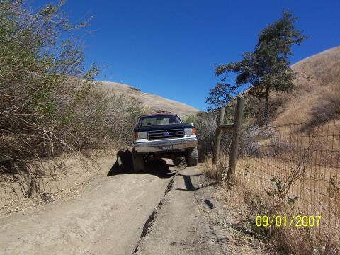 1991 Ford Bronco - A Ford F-Series truck navigates a dirt path on a sunny day.