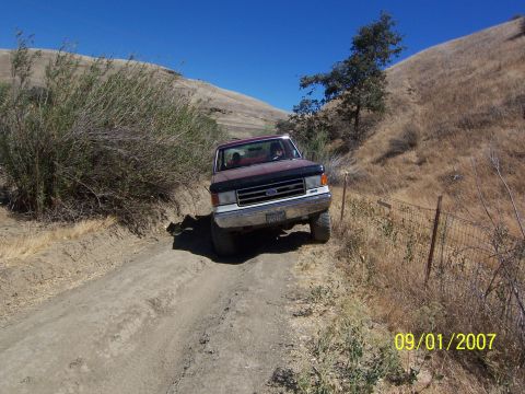 1991 Ford Bronco - 1991 Ford Bronco navigates a dusty, off-road trail under a clear blue sky.