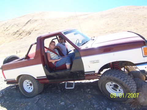 1991 Ford Bronco - A couple enjoys a ride in a lifted Ford Bronco on a dirt path.