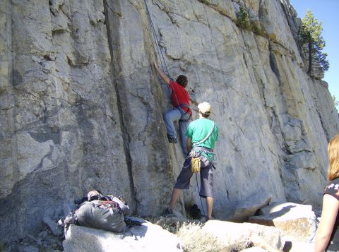 1986 Ford Bronco - Two people rock climbing on a large granite cliff face with gear laid out on the rocks below.