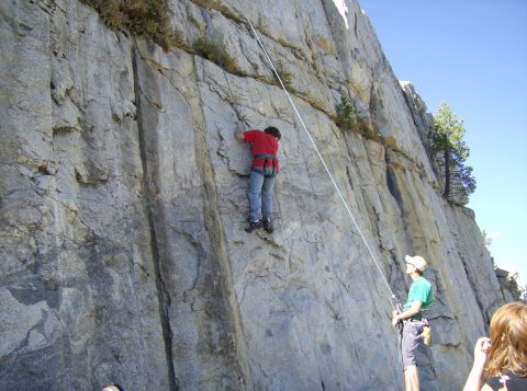 1986 Ford Bronco - Rock climbing activity with a climber ascending a steep cliff face under a clear blue sky.
