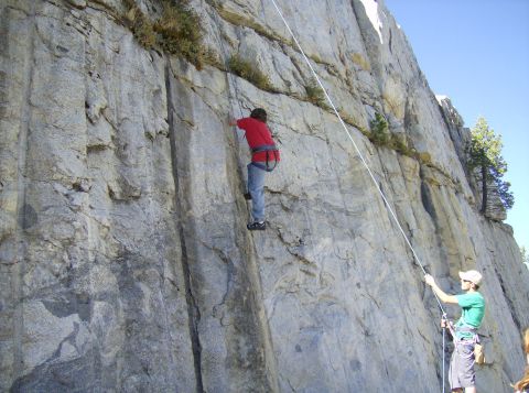 1986 Ford Bronco - Two people are rock climbing on a large cliff face with trees visible in the background.