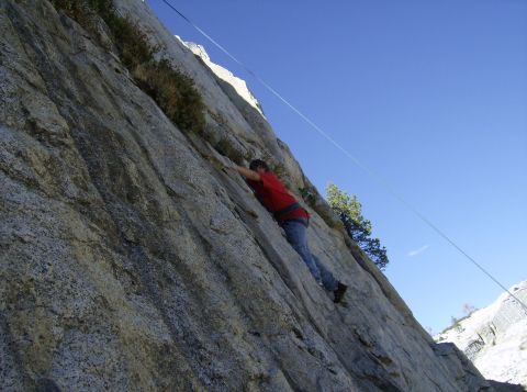 1986 Ford Bronco - A climber scales a large rock formation, with a rope extending upwards against the bright blue sky.