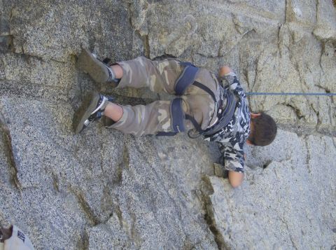 1986 Ford Bronco - A person in camouflage pants and a patterned shirt climbs a rock face, secured by a harness and rope.