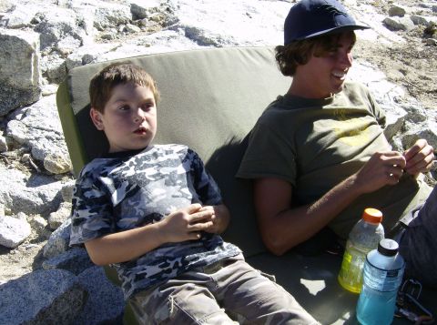 1986 Ford Bronco - Two individuals relax outdoors, with water bottles nearby, amidst a rocky landscape.