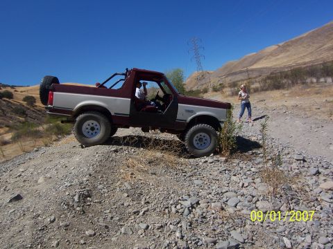 1991 Ford Bronco - A two-tone Ford Bronco is seen off-road on a sunny day with two people nearby.