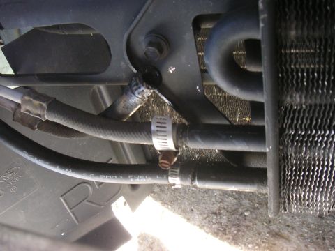 1996 Ford Crown Victoria - A transmission cooler line shows signs of a leak, with a hose clamp securing the damaged section near the radiator.