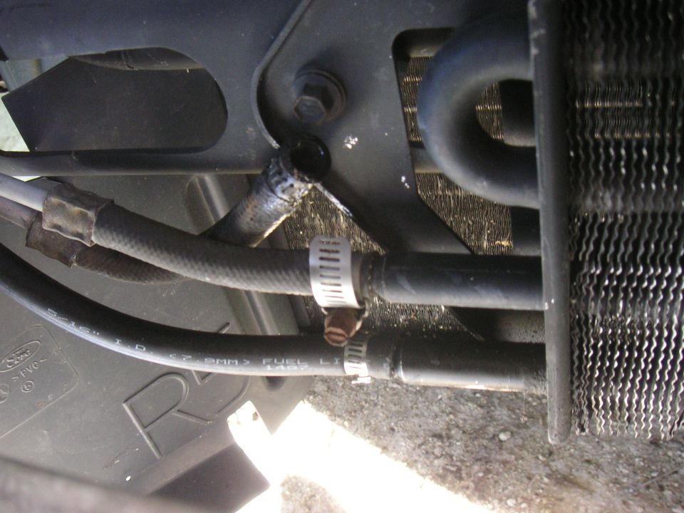 Rubber cooler and fuel lines joined with screw clamps beside a finned cooler core