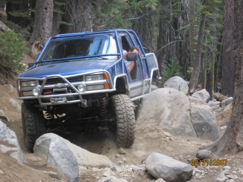 1994 Ford Bronco - A modified blue pickup truck navigates a rocky off-road trail.