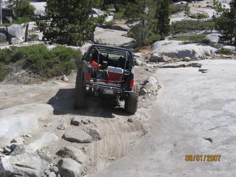 1994 Ford Bronco - Vehicle navigates a challenging rocky trail with trees and boulders in the background.