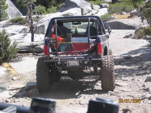 1994 Ford Bronco - Modified Ford Bronco navigates a challenging rocky terrain, showing its rear end and off-road equipment.