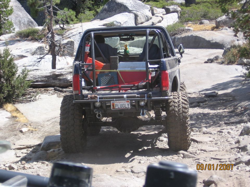 Cut-down Ford Bronco with roll cage climbing granite rock, rear view, PLUGLY plate