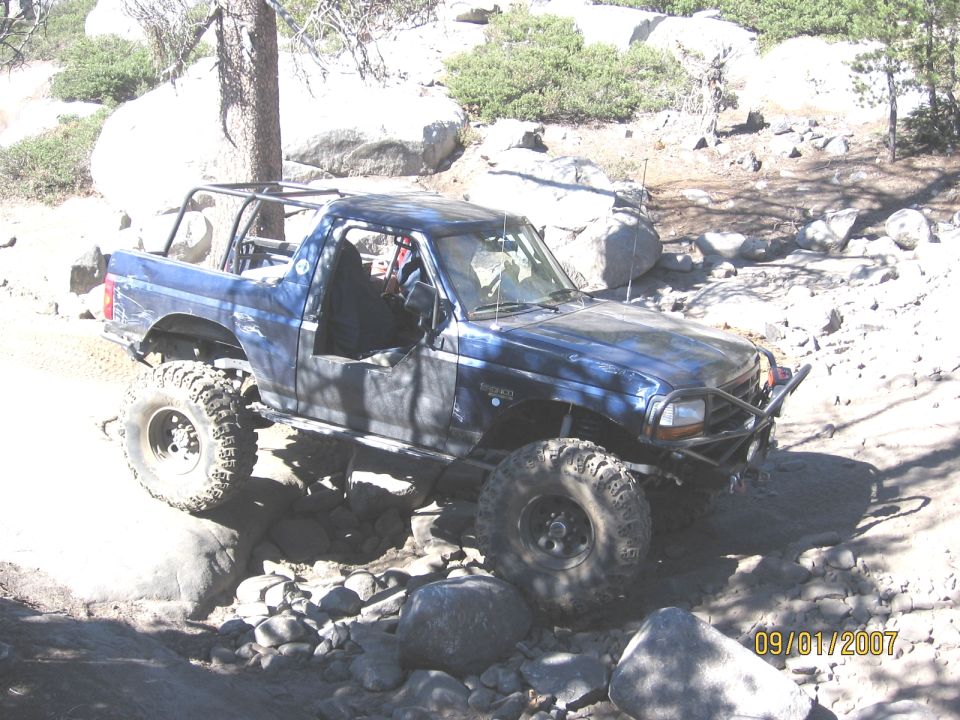Topless dark blue Ford Bronco with roll cage and winch bumper crawling granite boulders