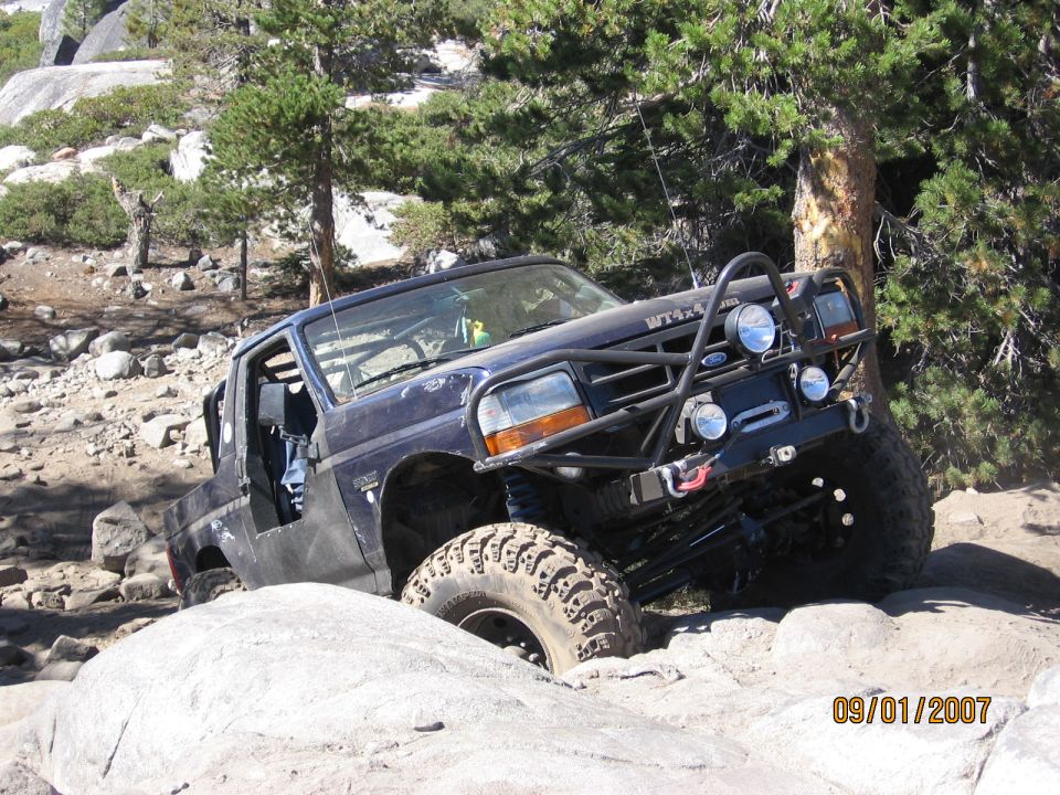 Dark blue Ford Bronco rock crawler with tube bumper and winch climbing granite boulders