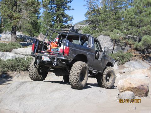 1994 Ford Bronco - This heavily modified SUV is navigating a rocky trail, equipped with a roll cage and oversized tires.