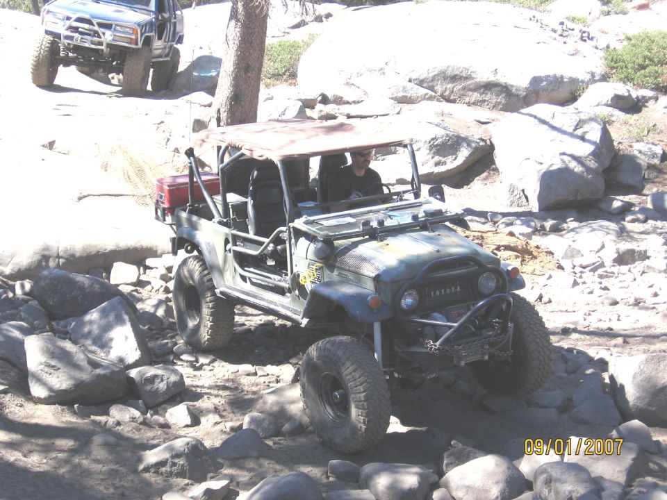 Olive-green Toyota FJ40 rock crawler with roll cage and no doors descending a rocky trail