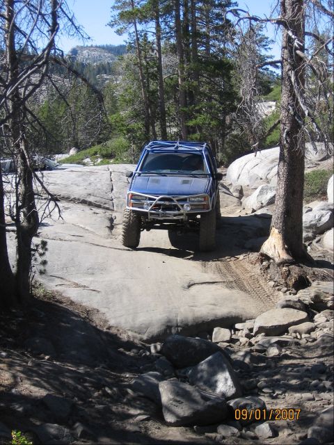 1994 Ford Bronco - This modified SUV navigates a challenging off-road path through a wooded, rocky terrain.
