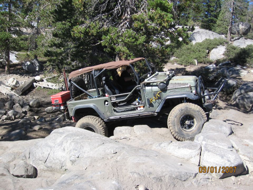 Olive green FJ40-style Land Cruiser with roll cage crawling granite in pines