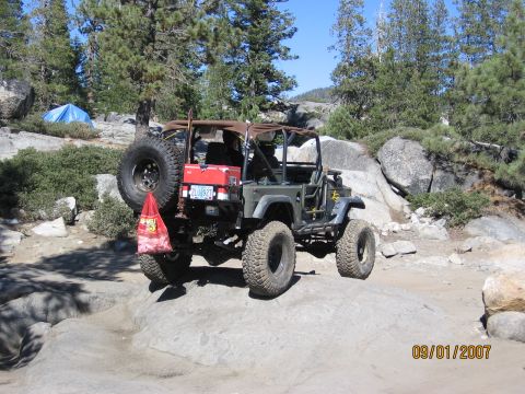 1994 Ford Bronco - Off-road Jeep navigates rocky terrain on a sunny day, with a tent visible in the distance.
