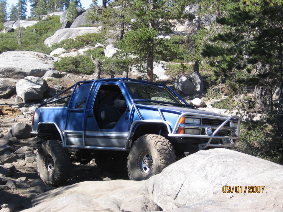 Blue caged doorless 4x4 rock crawler on boulders in a pine forest