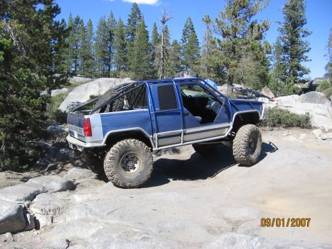 1994 Ford Bronco - Custom blue pickup truck navigates a rocky trail on a sunny day.