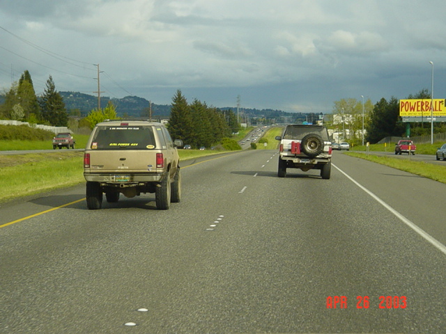 Two lifted SUVs with rear spare tires driving down a highway past a Powerball billboard