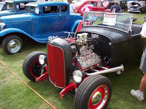 1997 Ford Mustang - A custom hot rod with a prominent V8 engine is displayed outdoors next to other classic vehicles.