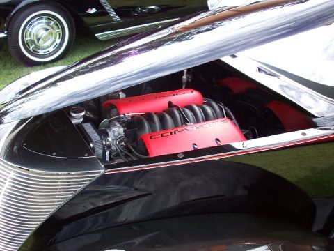1997 Ford Mustang - The engine compartment of a classic car reveals a modern Corvette engine, with another vintage vehicle parked nearby.