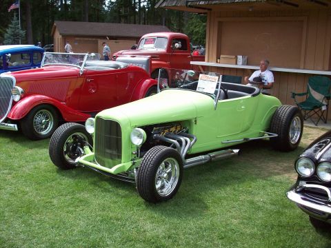 1997 Ford Mustang - A collection of classic cars, including a lime green hot rod and a red convertible, are displayed outdoors.