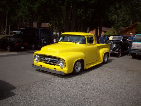 1997 Ford Mustang - A bright yellow 1956 Ford F-100 pickup truck is the main subject, with other vehicles visible in the background.